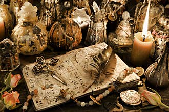 Magic ritual bottles with open witch book, quill and cross in candlelight on the table