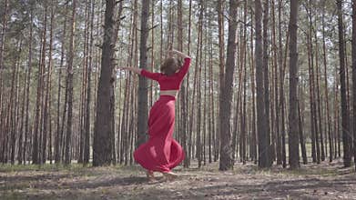 Confident pretty young woman in red dress dancing in the forest. Beautiful dancer dancing contemporary between the pines