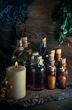 A witchery stuff: multiple tincture bottles, bunches of dry healthy herbs, stack of ancient ritual books, amulets, candles...