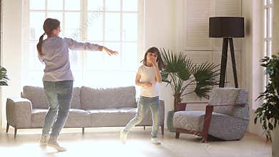 Active young mom and kid daughter dancing in living room