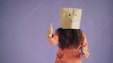 Girl with paper bag on head dancing showing thumbs-up showing like sign