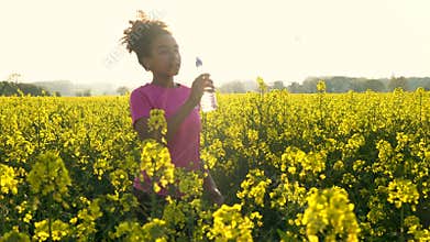 African American girl teenager female young woman drinking from water bottle and running or jogging in field of yellow flowers