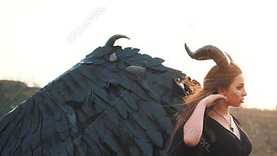 Lady dark vintage dress with huge heavy strong wings behind her back removes her long hair from her face with gentle