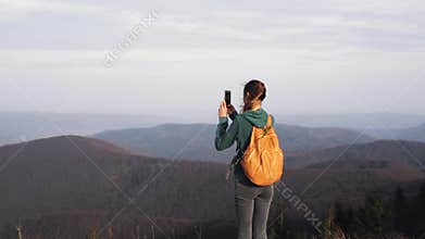 Woman hiker walking on edge of mountain ridge against background of sunset