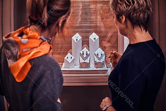 Customer and shop assistant are standing next to display with juwellery and choosing the right ornamentation