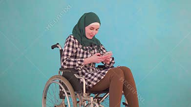 Young muslim woman disabled person in a wheelchair uses the phone on a blue background
