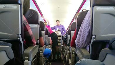 Stewardess at work, walking down aisle between rows of seats in aircraft cabin