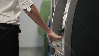 Young happy brunette woman withdrawing money from credit card at ATM in shopping mall,