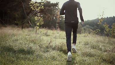 Slow motion. Man running up on tall grass hill. Back view tracking shot. Camera follows cross country sportsman runner.