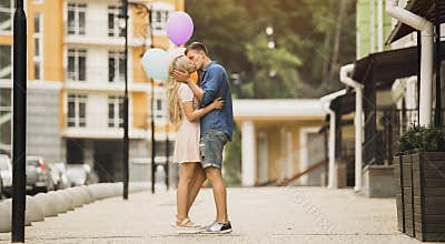 Passionate young couple kissing in street, holding colorful air balloons, dating
