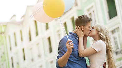 Happy couple with colorful air balloons kissing in street, tender relationship