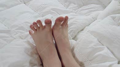 Delicate female feet moving toes playfully on white bedding