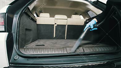 Man is cleaning wardrobe trunk of luxury vehicle with a vacuum cleaner - car detailing