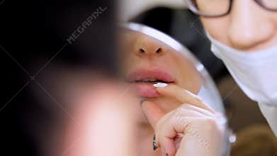 Medical office, beautiful woman looking in the mirror, doctor probes the patient`s lips after injections of hyaluronic