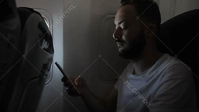Portrait of young man, who is using his smartphone in the aircraft.