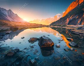 Mountains with illuminated peaks, stones in mountain lake at sunset