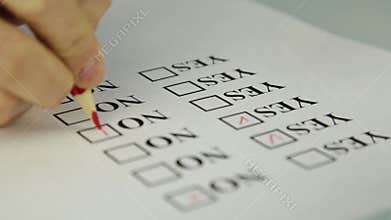 Close-up hand filling yes and no at the checklist box with red pencil