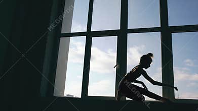 Silhouette of young girl dancer perfomance contemporary dance on windowsiil in dance studio indoors
