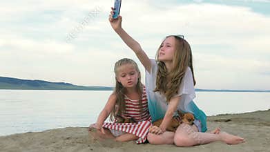 Two teenage children are sitting on the beach in phone.