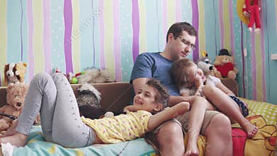 The young father and two little daughters play with soft toys, smile and laugh. father enjoys time with children