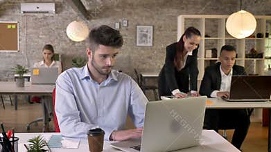 Young tired businessman is working in office, tapping on laptop, discussion on background, working concept, business