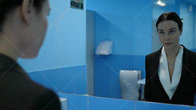 Apathy, frustrated young woman in public restroom takes off her eyeglasses and looks at herself in mirror