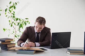 A man in a business suit works at a desk with a computer and books in the Office