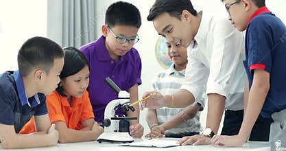Asian teacher expanding to student in biology class with microscope .