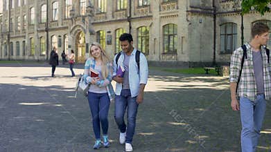 Mixed-race couples of students walking at university courtyard after classes