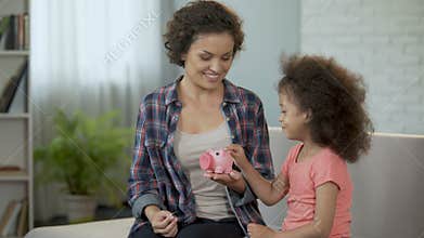 Mom and daughter throwing coins into piggy bank, saving money for presents