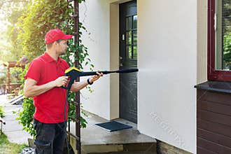 Worker with high pressure washer cleaning house facade