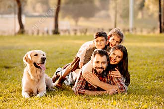 Happy family with two children lying in a pile on grass with dog sitting