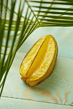 Star fruit carambola or star apple on green background with palm leaves, flat lay