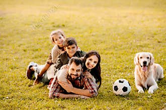 Happy family with two children lying in a pile on grass with dog sitting