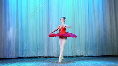 Ballet rehearsal, on the stage of the old theater hall. Young ballerina in red ballet tutu and pointe shoes, dances