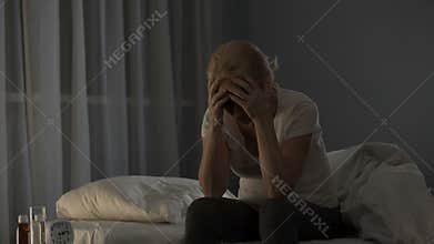 Lady sitting on bed, unable to fall asleep due to severe migraine and bad pain