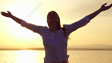 Woman raising arms up at sunset on lake. Female outstretching hands at golden hour in slow motion
