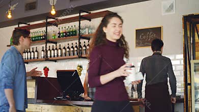 Young people are buying coffee-to-go in nice local cafe and paying with smartphone while friendly workers are greeting