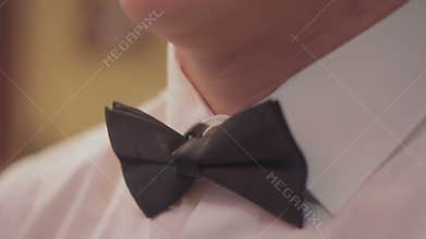The man is adjusting his bow tie, preparing for the holiday. Closeup