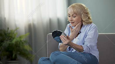 Mature woman looking into a hand mirror, enjoying reflection. Anti-age cosmetics