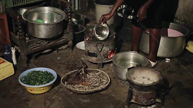 KENYA, KISUMU - MAY 20, 2017: Close-up view of young african woman preparing dinner, boils water on burning coals for