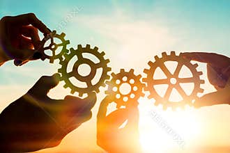 Four hands of businessmen collect gear from the gears of the details of puzzles. against the sunset.