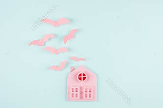 Halloween background - pink house and flock fly bats as cut cartoon on pastel mint blue paper background.