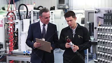 Business owner in factory discussing component with engineer