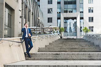 handsome young businessman in stylish suit with coffee to go talking by phone on stairs