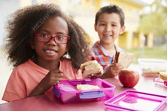 Two young school kids eating their packed lunches together
