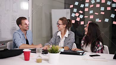Positive young people laughing while working together during brainstorming sitting at the big white office table behind
