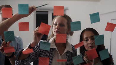 Team of three young people - young business people while working together during brainstorming and standing behind glass