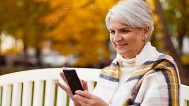 Happy senior woman with smartphone at autumn park