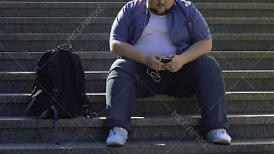 Lazy man sitting on stairs, listening to music and chatting with friends online